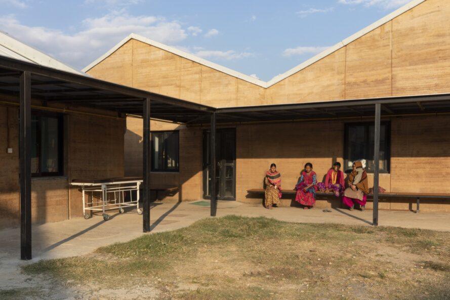 people sitting on a bench along a rammed earth wall